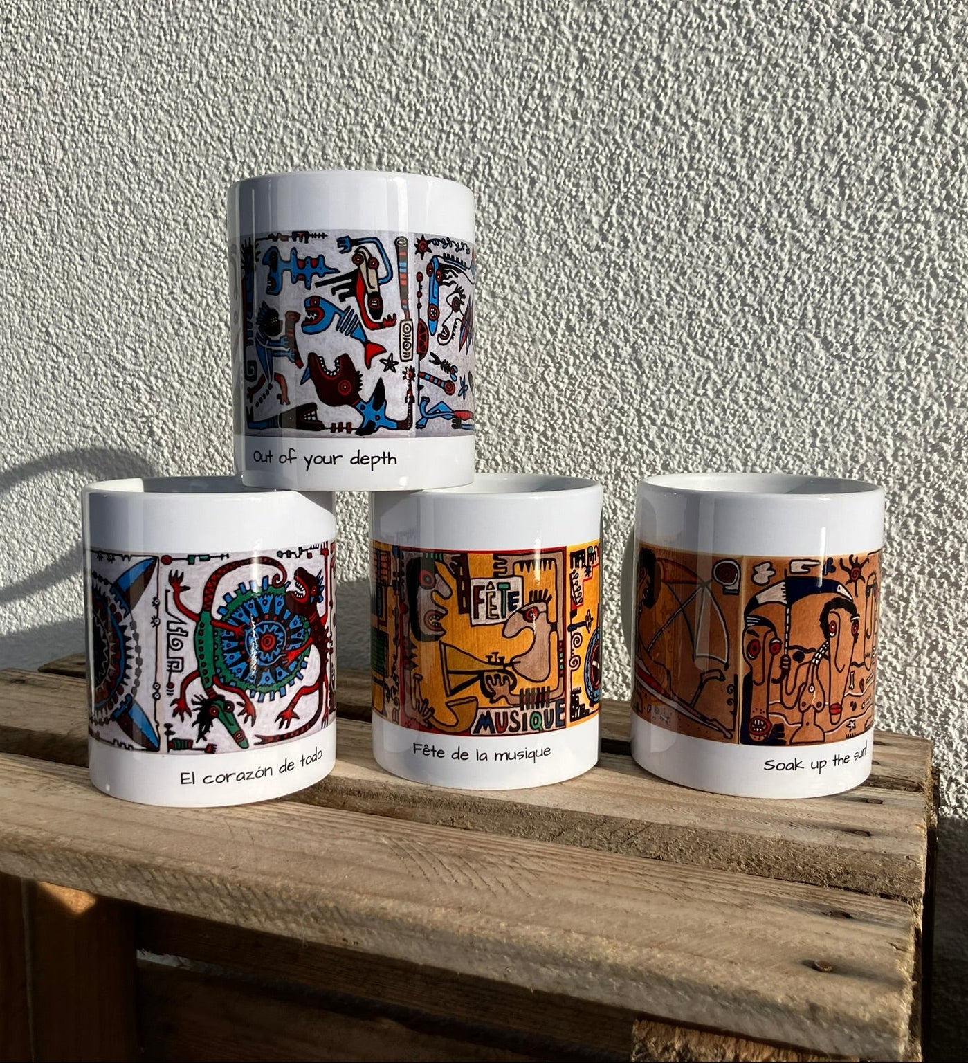 Cztery kubki ze wzorami z ręcznie malowanych kafli na tle jasnej ściany. Każdy kubek zawiera trzy grafiki, które składają się na jedną historię.
