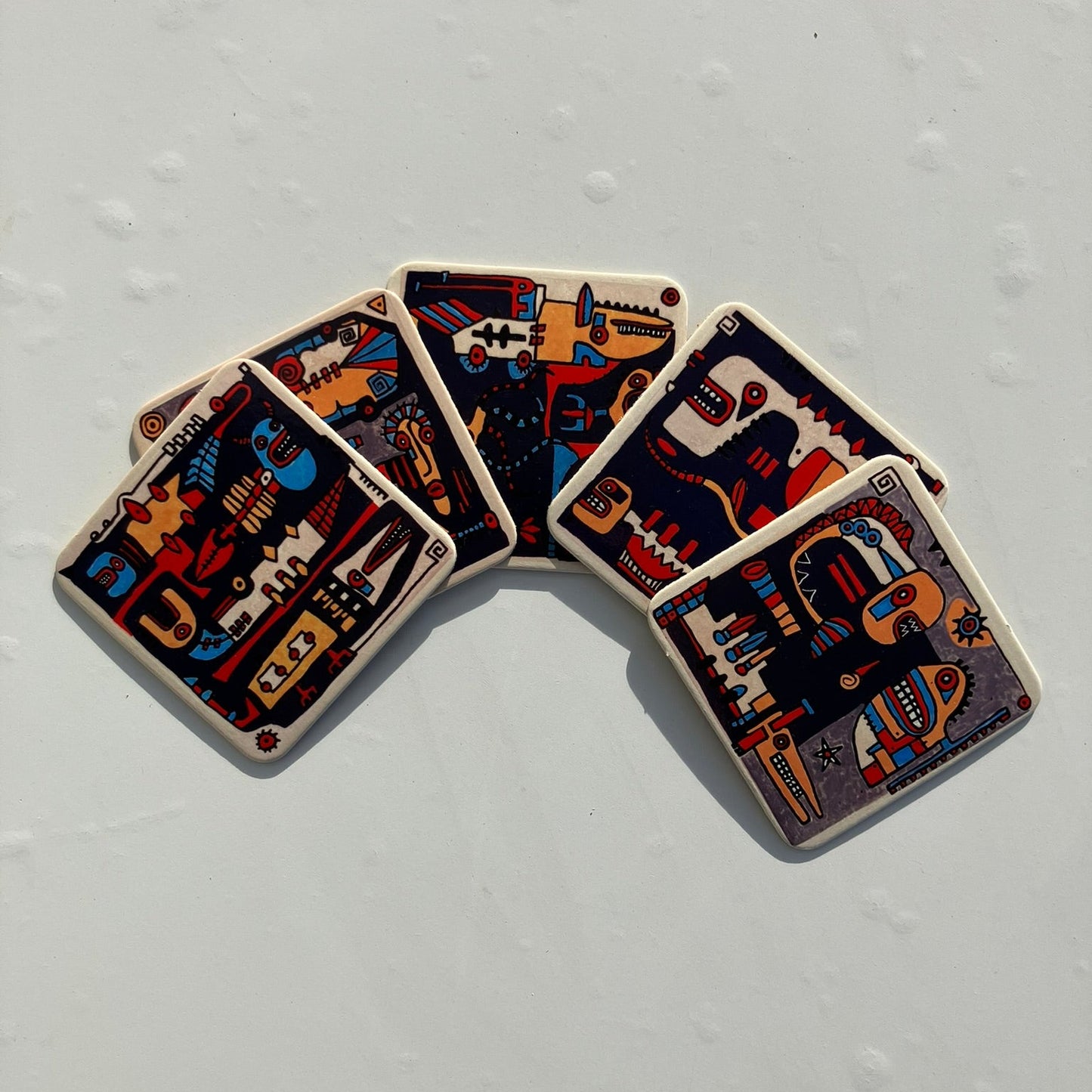 Pięć podkładek z artystycznym, abstrakcyjnym designem ułożonych w wachlarz na jasnym tle. 