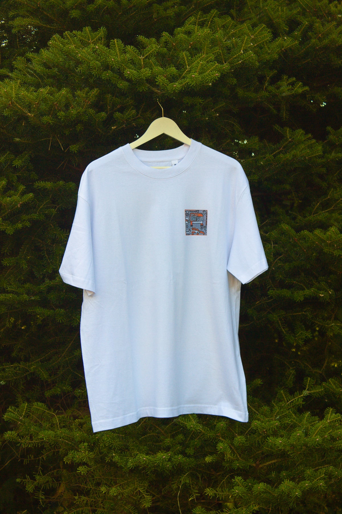 Biały t-shirt z małą, kolorową grafiką abstrakcyjną umieszczoną na piersi.