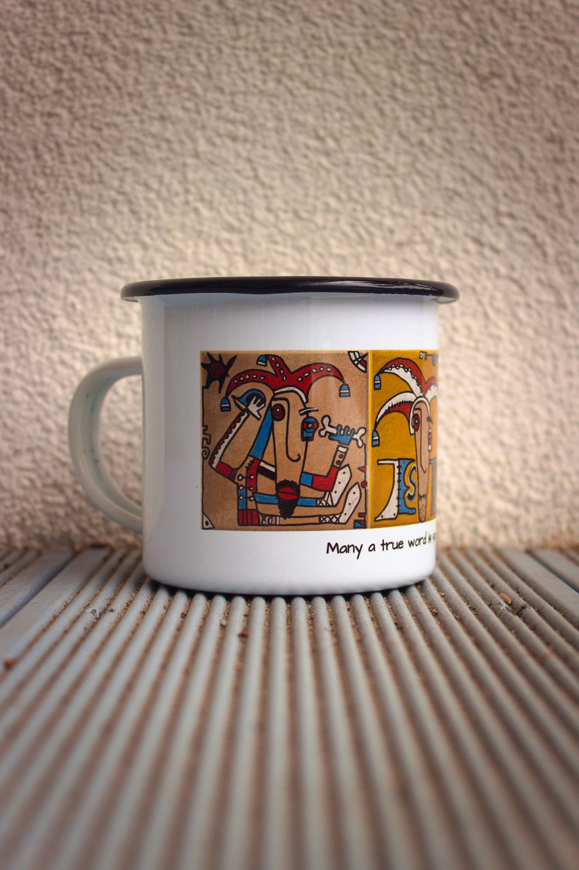 Biały kubek stalowy z autorskim motywem kaflowym „Jester”, widok na lewą stronę kolorowego nadruku.