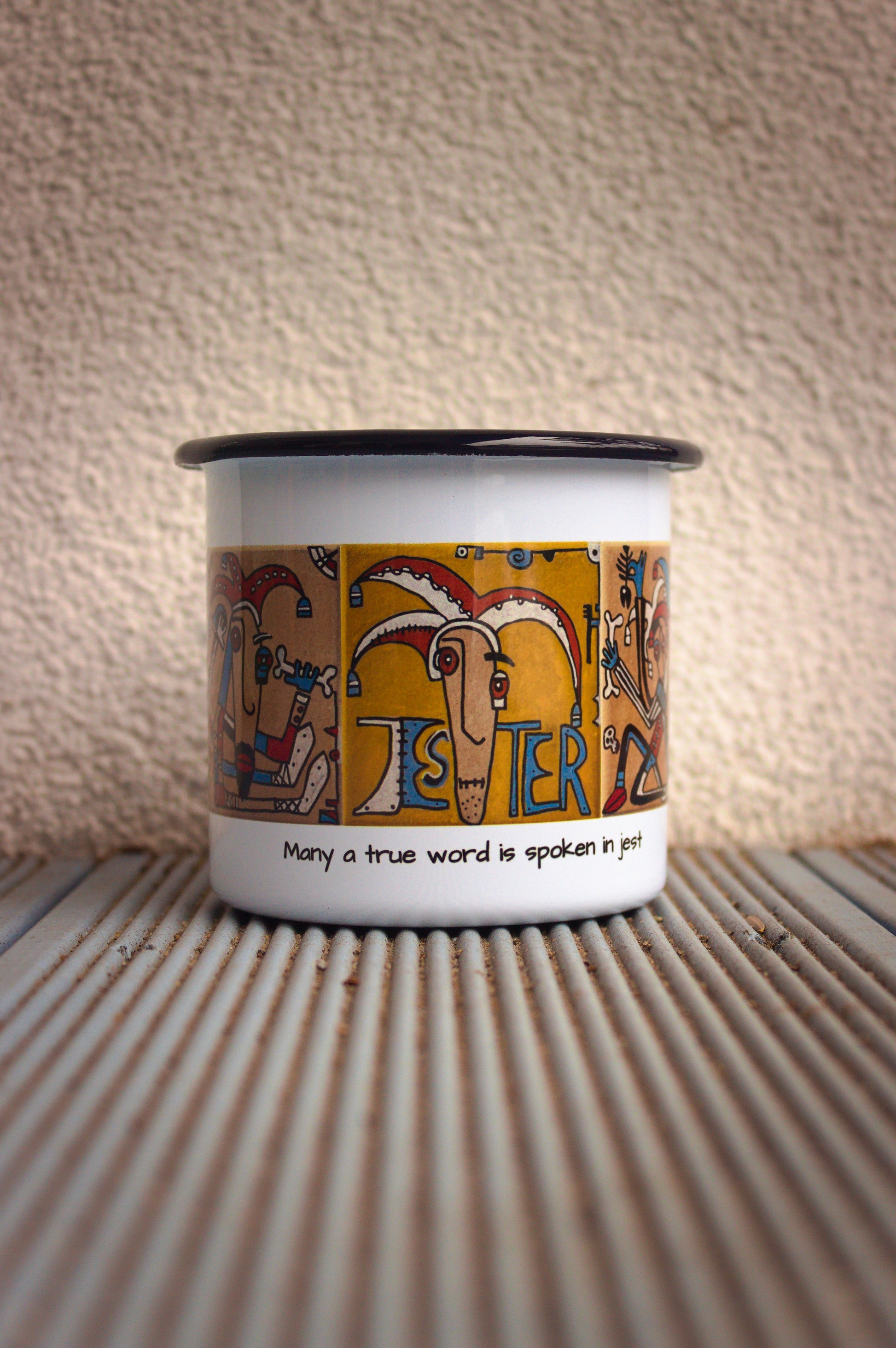 Kubek stalowy retro z grafiką błazna i napisem „Many a true word is spoken in jest”.