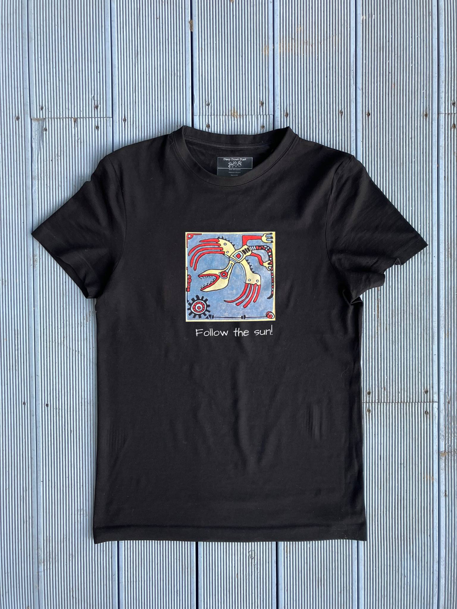 Czarna koszulka unisex z nadrukiem ręcznie malowanego kafla "Follow the sun". Grafika w stylu etno z motywem czerwonego stworzenia i napisem pod spodem.