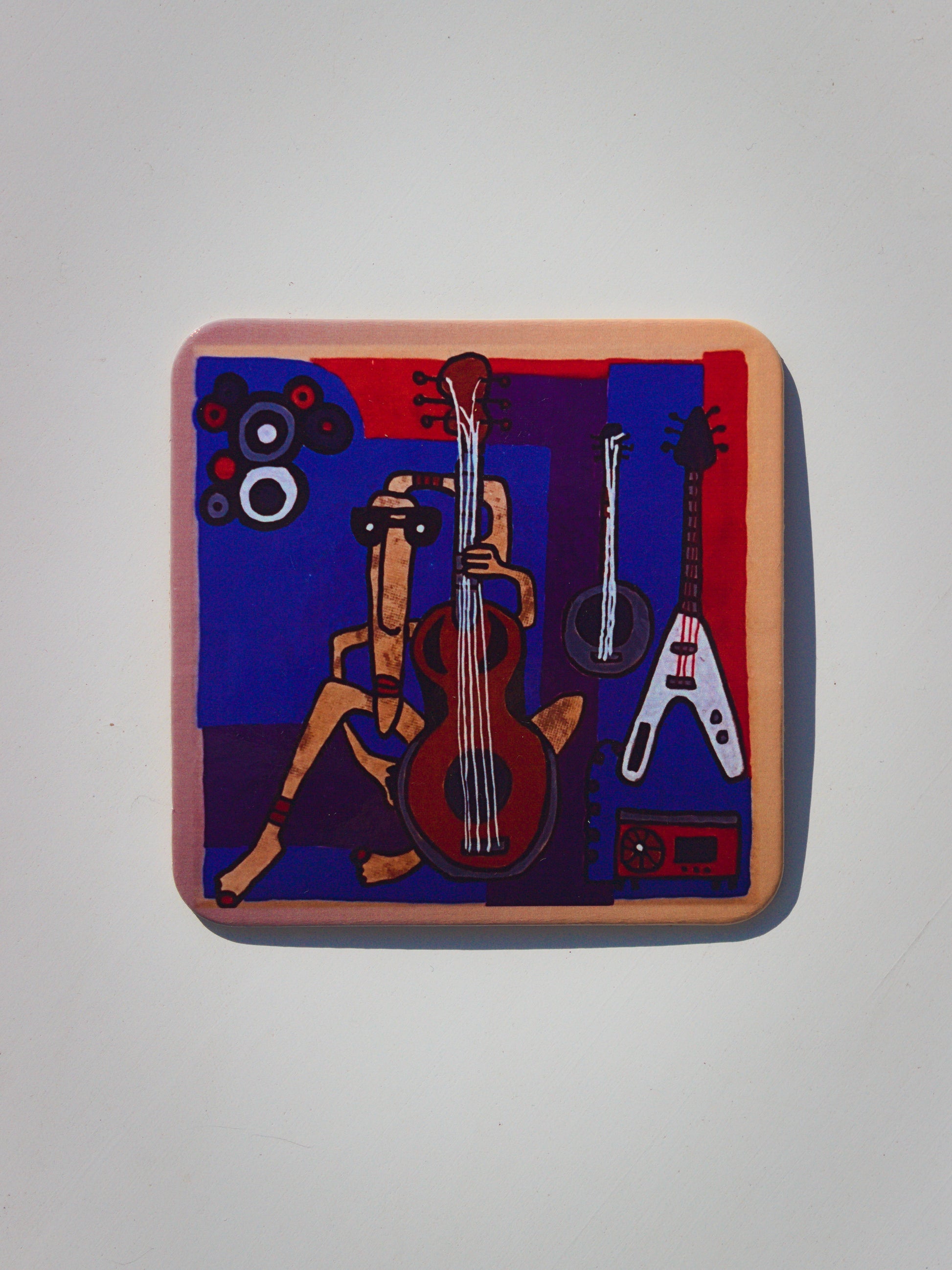 Podkładka korkowa z surrealistyczną grafiką muzykantki grającej na gitarze w otoczeniu innych gitar, ciemnoniebieskie tło.