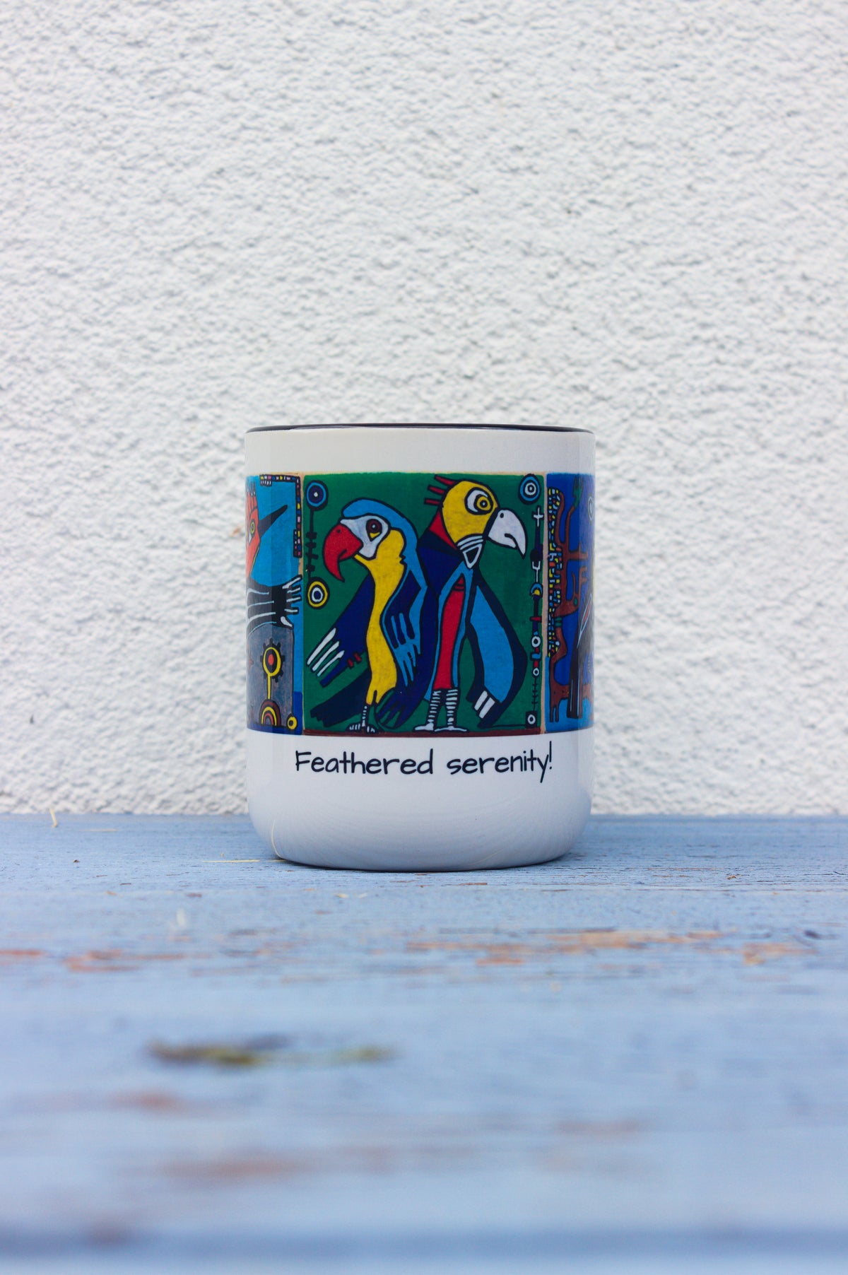 Ceramiczny kubek z kolorowymi papugami i napisem Feathered serenity od przodu.
