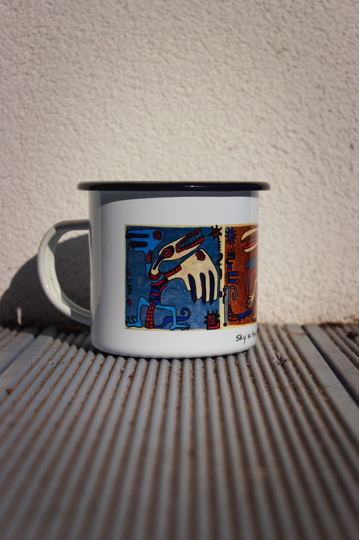 Kubek turystyczny stalowy z nadrukiem surrealistycznej postaci o niebieskich skrzydłach, widok z boku.