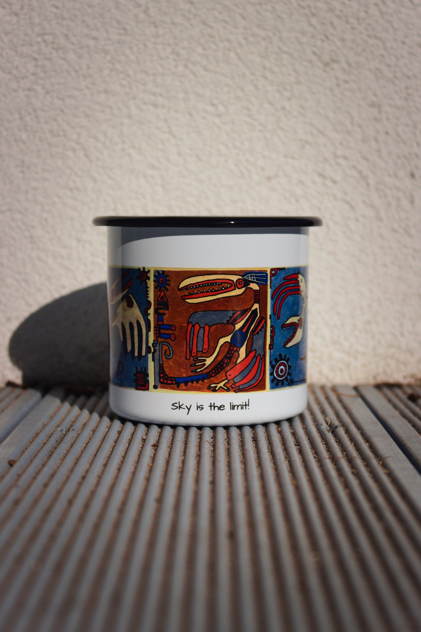 Biały kubek stalowy retro z autorską grafiką kaflową i napisem „Sky is the limit!” na tle ryflowanych desek.
