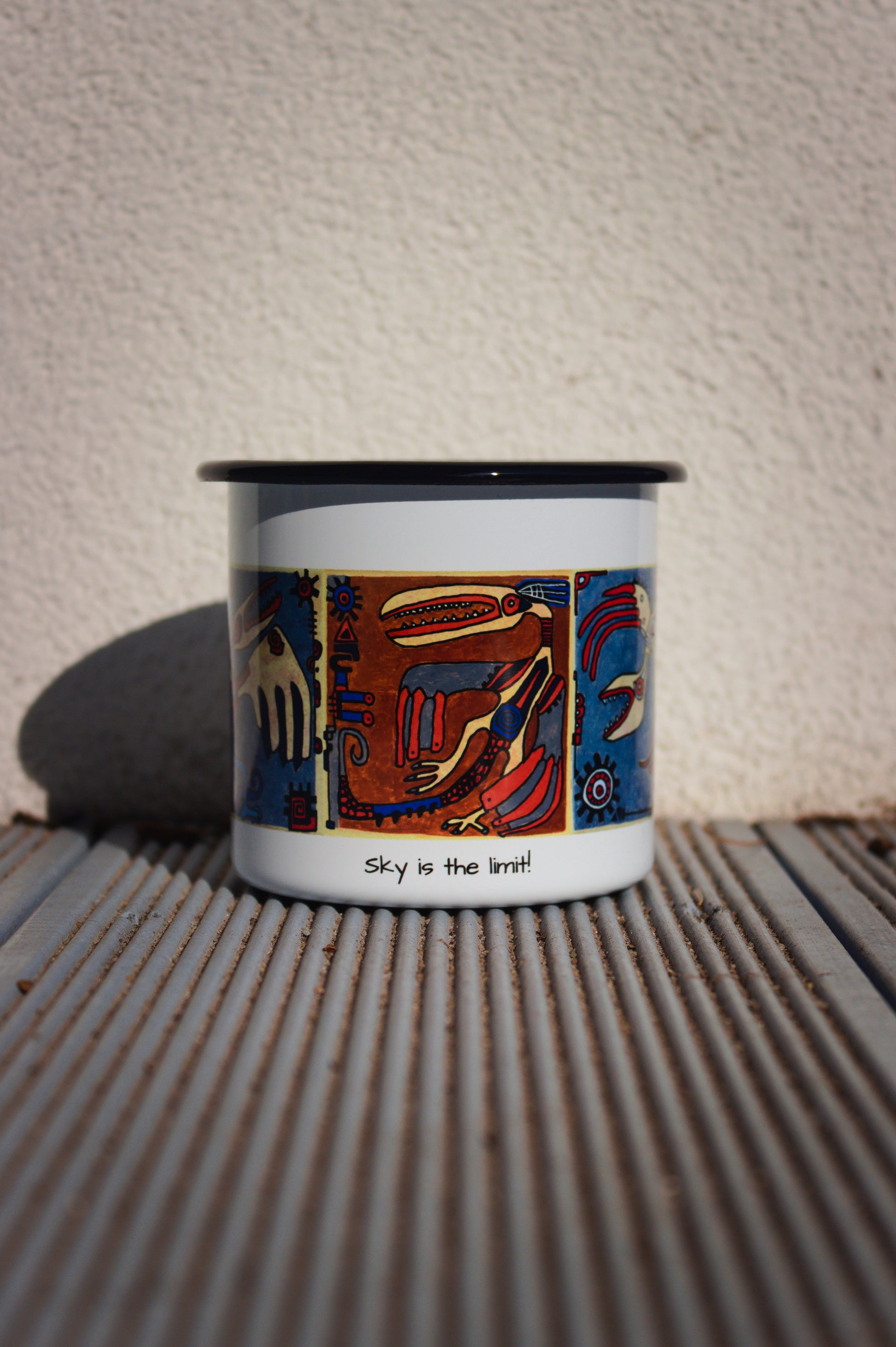 Biały kubek stalowy retro z autorską grafiką kaflową i napisem „Sky is the limit!” na tle ryflowanych desek.